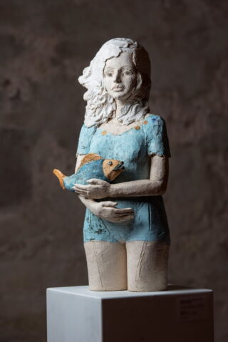 Skulptur aus Keramik. Frau hält Fisch auf dem Arm